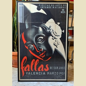 May include: Framed vintage poster featuring a stylized face against a black backdrop. The word "fallas" is in red script, with text indicating "Valencia, March 1957". The poster is framed in a black wooden frame.
