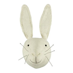 Può includere: Una testa di coniglio in feltro bianco per decorare la parete, con occhi neri e un sorriso cucito. Il coniglio ha orecchie lunghe e cadenti e una texture soffice.