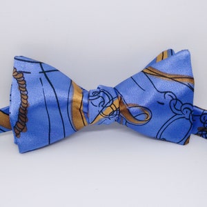 May include: A blue bow tie with a gold and black nautical pattern. The pattern includes ropes, anchors, and other nautical symbols.