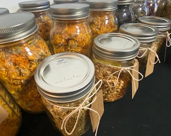 Peut inclure: Une collection de bocaux en verre remplis de fleurs et d'herbes séchées. Les bocaux ont des couvercles argentés et sont attachés avec de la ficelle et des étiquettes en papier brun.