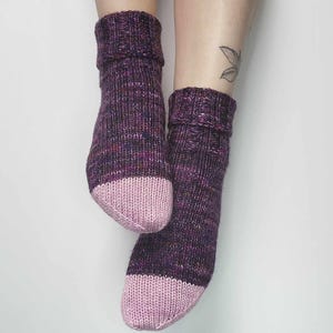 Peut inclure: Une paire de chaussettes en tricot violet et rose avec un orteil et un talon roses. Les chaussettes sont faites avec un fil moucheté.