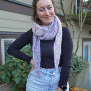 May include: A person wearing a black long-sleeved shirt with a purple and pink scarf. They are wearing blue jeans and a black watch with a round face.