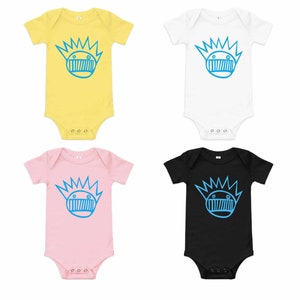 May include: Four baby onesies in different colors: yellow, white, pink, and black. Each onesie features a blue cartoon character with a crown of spikes and a mouth.