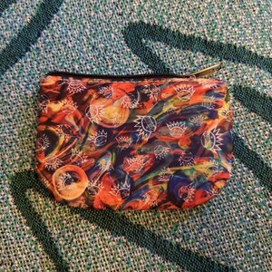 May include: A small, colorful zippered pouch with a psychedelic print of white eyes with sunbursts on a background of orange, red, blue, and yellow swirls.