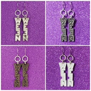 May include: Four pairs of dangle earrings with the word "WEEN" spelled vertically on each earring. The earrings are silver, black, bronze, and white.