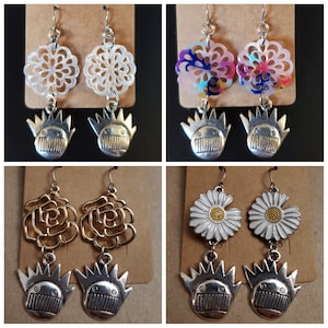 May include: Four pairs of earrings with a variety of designs. The earrings feature a white, pink, and blue floral design, a gold rose design, and a silver skull design.