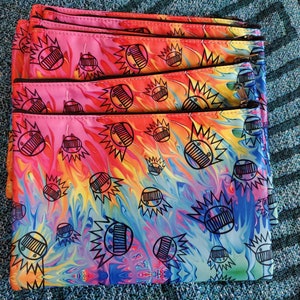 May include: A stack of six colorful zippered pouches with a tie-dye pattern and black and white graphic designs. The pouches are made of a soft, durable fabric and are perfect for storing small items.