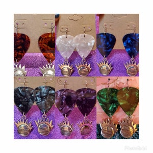 May include: A set of 10 pairs of earrings featuring guitar picks with various patterns and a silver charm with a crown and a face. The patterns include tortoise shell, white, blue, black, purple, and green.
