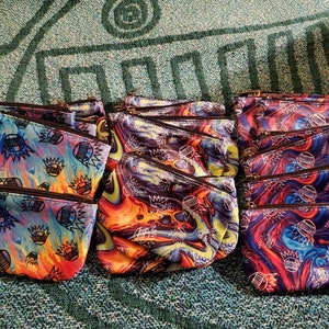 May include: A group of colorful zippered pouches with a swirling, abstract pattern. The pouches are made of a soft, fabric-like material and feature a zipper closure. The pattern includes shades of blue, red, yellow, and black.