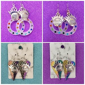 May include: A collection of handmade earrings. The earrings feature a silver-colored charm with a crown and face design. Some earrings have clear hoops with colorful gems, while others have heart-shaped pendants with a rainbow metallic finish.