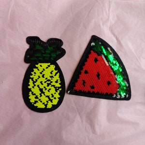 Può includere: Due toppe termoadesive colorate, una a forma di ananas con paillettes gialle e verdi, l'altra a forma di fetta di anguria con paillettes rosse, verdi e nere.
