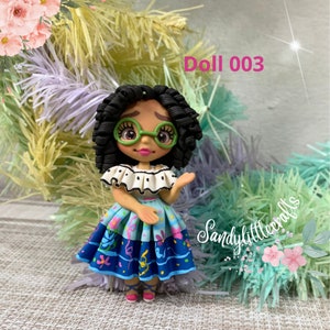 May include: A handmade doll featuring black curly hair, green spectacles, and a vibrant dress. The doll's top is white with black polka dots, and the skirt is blue with floral and ribbon patterns. The text "Doll 003" is displayed.