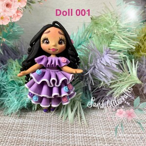 May include: A handmade doll with black curly hair and a purple tiered dress decorated with small flowers. The doll has a painted face and is labelled "Doll 001". The doll is a handmade craft.