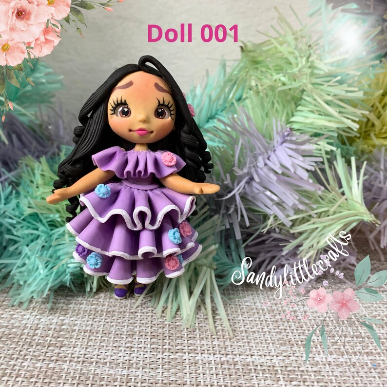 May include: A handmade doll with black curly hair and a purple tiered dress decorated with small flowers. The doll has a painted face and is labelled "Doll 001". The doll is a handmade craft.