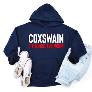 Puede incluir: Una sudadera con capucha azul marino con un gráfico blanco que dice "Coxswain The Coach's Evil Minion" en letras rojas y blancas.