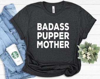 May include: A dark grey t-shirt with the text "BADASS PUPPER MOTHER" printed in white.
