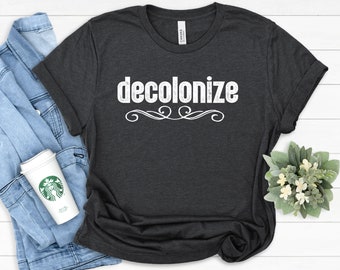 May include: A dark gray t-shirt with the word "decolonize" printed in white on the front. The shirt has a distressed look and is made of a soft, comfortable fabric.