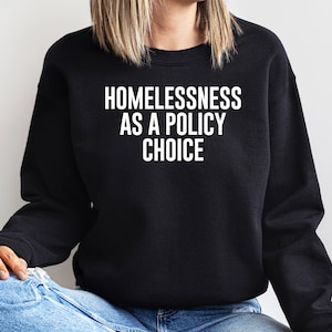 Puede incluir: Una sudadera negra con el texto "Homelessness as a policy choice" impreso en blanco.