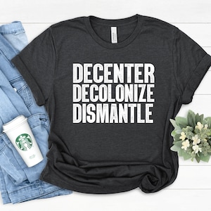May include: A dark gray t-shirt with the words "DECENTER DECOLONIZE DISMANTLE" printed in white.