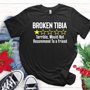 May include: Black t-shirt with the text "BROKEN TIBIA" and a one-star rating. The text below the rating says "Terrible, Would Not Recommend To a Friend."