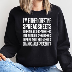 May include: Black sweatshirt with white text: "I'M EITHER CREATING SPREADSHEETS LOOKING AT SPREADSHEETS TALKING ABOUT SPREADSHEETS THINKING ABOUT SPREADSHEETS DREAMING ABOUT SPREADSHEETS". The sweatshirt is worn by a person.
