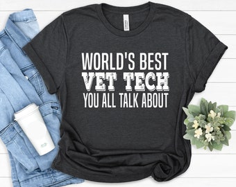 May include: A dark heather gray short-sleeve t-shirt featuring the white text "WORLD'S BEST VET TECH YOU ALL TALK ABOUT" printed in a bold, distressed font across the center of the chest. The shirt has a crew neckline and a standard fit.
