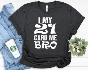 Op de afbeelding: Een donker antracietgrijs T-shirt met korte mouwen en de witte tekst I MY 21 CARD ME BRO in een vetgedrukt, gestileerd lettertype in het midden van de borst. Het T-shirt heeft een ronde hals en een standaard pasvorm met zichtbare textuur.