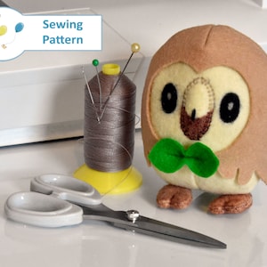 May include: A brown and beige felt owl plush toy with a green bow tie. The owl is sitting on a white surface next to a spool of gray thread and a pair of silver scissors. The text "Sewing Pattern" is visible in the background.