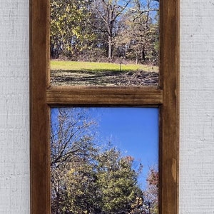 May include: A wooden picture frame with four separate windows, each displaying a different season of the same forest scene. The top window shows a forest in summer with a large tree in the center. The second window shows the forest in fall with yellow and orange leaves. The third window shows the forest in winter with bare branches. The bottom window shows the forest in spring with new green leaves.