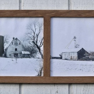 May include: A wooden picture frame with two separate windows, each displaying a black and white photograph of a barn in a snowy field. The barn on the left is a traditional style with a silo, while the barn on the right is a more modern style with a tall tower.