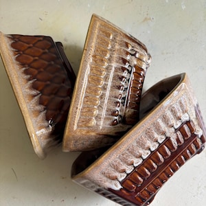 May include: Three ceramic bowls with a glossy brown glaze and a textured, cream-colored drip pattern along the rims. Each bowl features a distinct embossed design, including a diamond pattern on one and vertical ribbed columns on the others.
