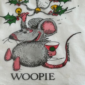 May include: A white napkin with a cartoon illustration of a mouse holding a cocktail. The mouse is gray with pink ears and feet, and the text "WOOPIE" is printed below. Above the mouse are holly and light bulb decorations.
