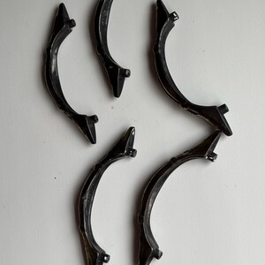 May include: Five curved, black metal drawer pulls arranged in a scattered pattern. Each handle features a slender, arched design with two small mounting posts extending from the underside, showing a dark, slightly weathered finish throughout.