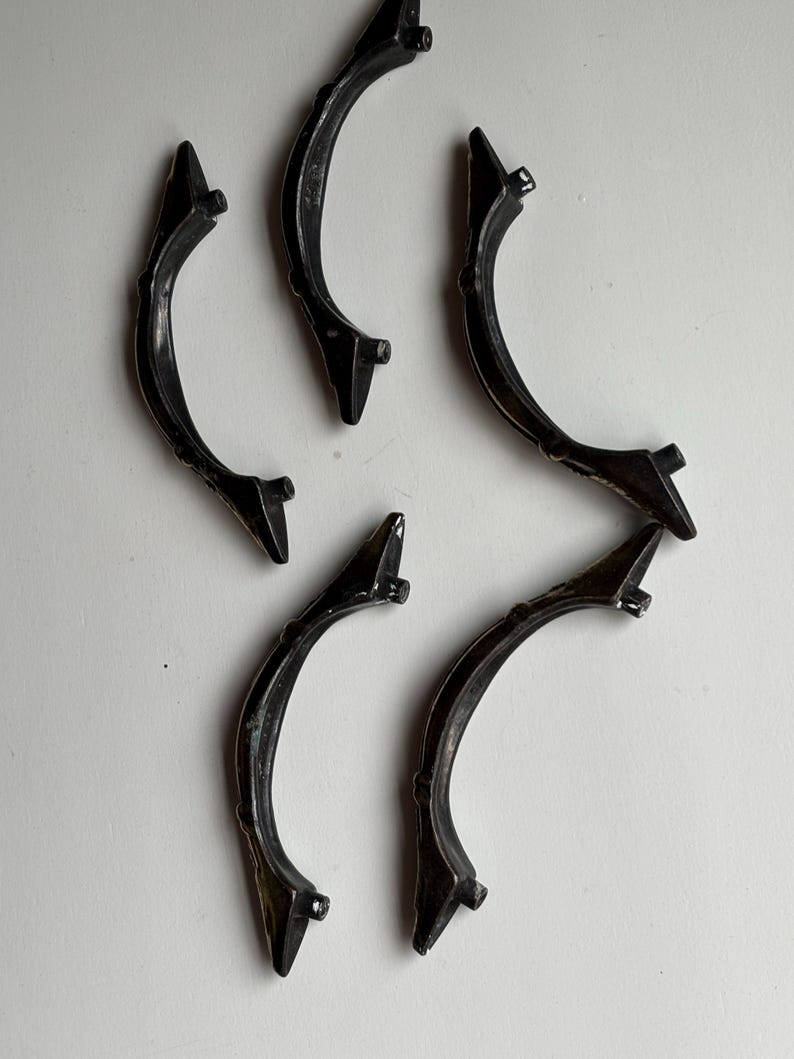 May include: Five curved, black metal drawer pulls arranged in a scattered pattern. Each handle features a slender, arched design with two small mounting posts extending from the underside, showing a dark, slightly weathered finish throughout.