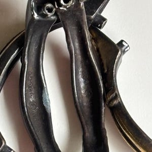 May include: A set of three dark metallic drawer pulls with a curved, elongated shape. Each handle features two protruding screw posts on the back for mounting. The metal surface shows signs of wear and includes the embossed text 440019.