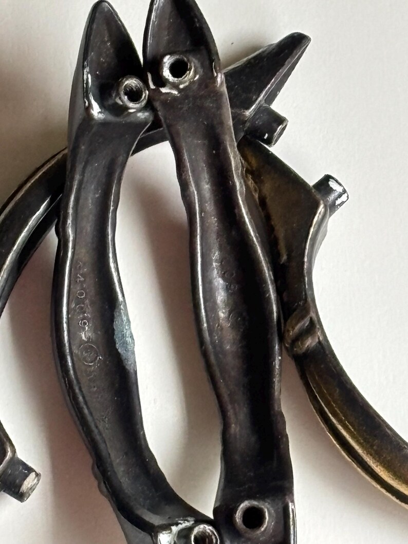 May include: A set of three dark metallic drawer pulls with a curved, elongated shape. Each handle features two protruding screw posts on the back for mounting. The metal surface shows signs of wear and includes the embossed text 440019.