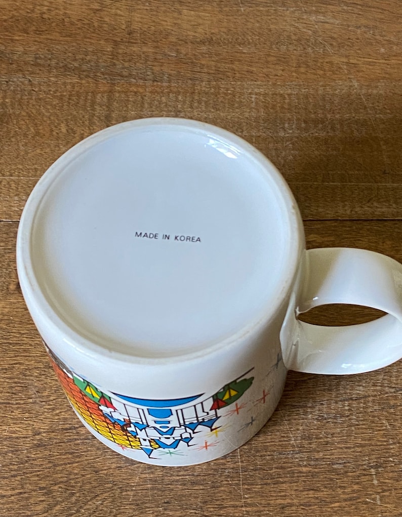 Puede incluir: Taza de cer&aacute;mica blanca con un dise&ntilde;o colorido y el texto "MADE IN KOREA" en la parte inferior.