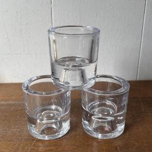 May include: Three clear glass candle holders with a small round base. The candle holders are stacked on top of each other.