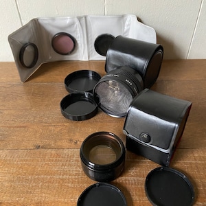 May include: A set of black camera lens filters and cases. The filters are in various sizes and are all black. The cases are also black and have a zipper closure.