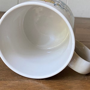 Puede incluir: Taza de cer&aacute;mica blanca con un dise&ntilde;o colorido de un edificio con un techo amarillo y ventanas azules. La taza est&aacute; vac&iacute;a y el interior es blanco.