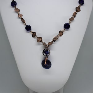 May include: A copper necklace with a hammered metal chain and dark blue glass beads. The necklace has a pendant with a large, round, dark blue glass bead.