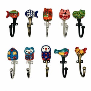 May include: A collection of decorative wall hooks featuring colorful, hand-painted ceramic animal and object designs. The hooks include fish, cats, owls, birds, a house, and a chicken, each with a unique design and metal hook.