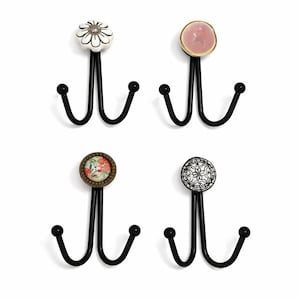 Pode incluir: Quatro ganchos de parede decorativos com armações de metal preto e botões de cerâmica exclusivos. Os botões apresentam uma flor branca, uma pedra rosa, um design floral e um padrão em preto e branco. Cada gancho tem três ganchos curvos.