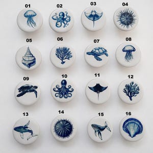 Peut inclure: Ensemble de seize boutons de placard en céramique blanche avec des motifs bleus de la vie marine. Les motifs incluent une méduse, une pieuvre, une raie, un oursin, un coquillage, du corail, une tortue de mer et une baleine.