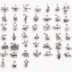 Puede incluir: Una colección de pequeños dijes de metal plateado en varias formas de animales y objetos. Los dijes incluyen una libélula, un ciervo, una mariposa, una ardilla y un ancla, entre otros. Adecuado para la fabricación de joyas o proyectos de manualidades.