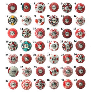 May include: A collection of 42 decorative ceramic cabinet knobs in various designs. The knobs are primarily red and white, with floral, geometric, and abstract patterns. Each knob has a silver-toned metal base for attachment.