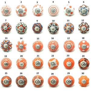 May include: A collection of thirty decorative ceramic cabinet knobs. The knobs are round, with various patterns and colors, including white, orange, and blue. Each knob has a silver-colored metal base.