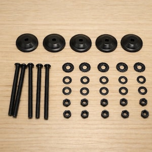 May include: A hardware kit with black components, including five round, flat-topped pieces, several long screws, washers, and nuts. The items are arranged on a light wood-grain surface.