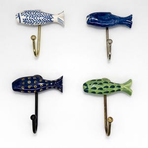 May include: Four ceramic fish-shaped wall hooks in blue, green, and white. The fish have different patterns and are mounted on metal hooks. These decorative hooks are suitable for a nautical or coastal themed interior, and are ideal for hanging items.