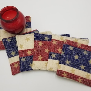 May include: Set of six red, white, and blue fabric coasters with a gold star pattern. The coasters are arranged in a row with a red candle holder on top of the first coaster.